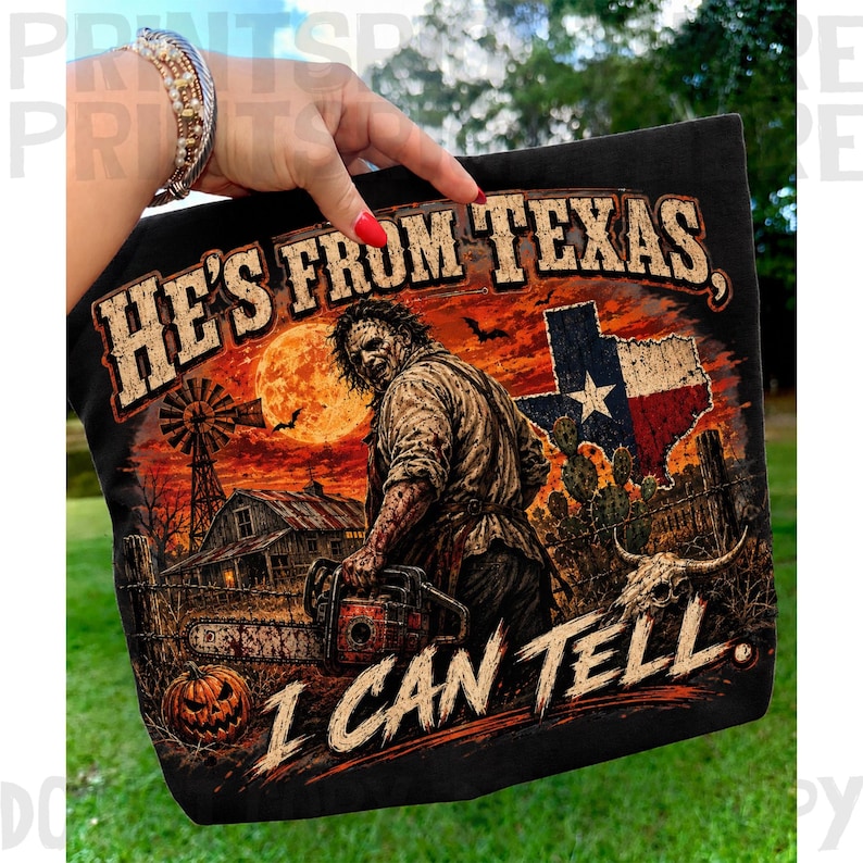 Puede incluir: Una camiseta negra con un estampado gr&aacute;fico de un personaje de terror sosteniendo una motosierra en un paisaje rural de Texas. El dise&ntilde;o incluye un granero, un molino, un cactus, una calavera, una luna llena y la bandera de Texas. Texto: HE'S FROM TEXAS, I CAN TELL.