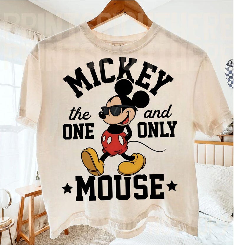 May include: Cream-coloured t-shirt featuring a graphic of Mickey Mouse wearing sunglasses, with the text "Mickey the One and Only Mouse" in black. Mickey is depicted in his classic red shorts, yellow shoes, and white gloves.