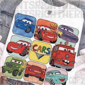 May include: White sweatshirt featuring a colorful graphic of various cartoon cars. The design includes images of Lightning McQueen, Mater, and other characters from the animated movie "Cars". The word "CARS" is also displayed.