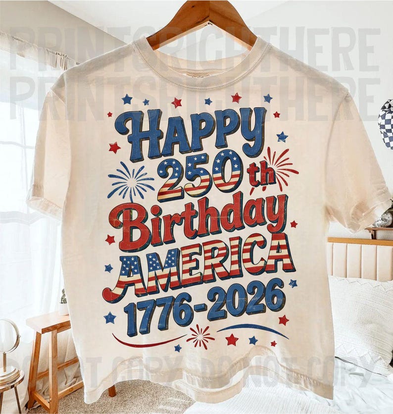 May include: Cream-colored t-shirt with a patriotic design celebrating America's 250th birthday. The design features the words "Happy 250th Birthday AMERICA 1776-2026" in red, white, and blue, with star and firework accents.