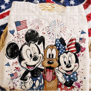 Könnte beinhalten: Cremefarbenes Sweatshirt mit Mickey Mouse, Pluto und Minnie Mouse, dekoriert mit amerikanischen Flaggen und Feuerwerk. Die Charaktere tragen patriotische Kleidung in Rot, Weiß und Blau. Ideal für den Unabhängigkeitstag.