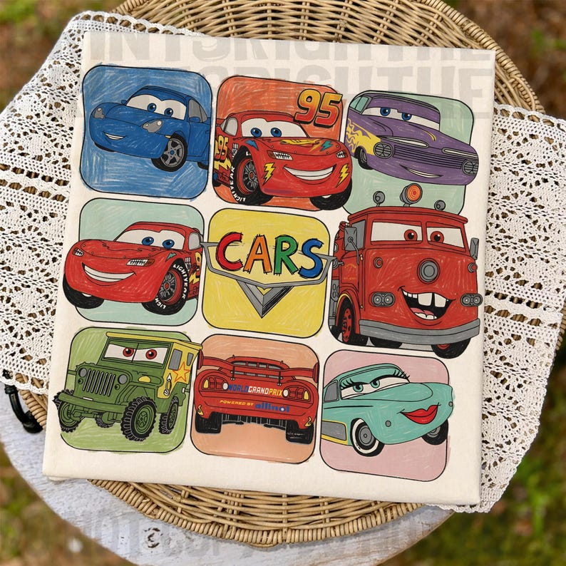 May include: Square canvas art featuring colorful cartoon cars in individual squares. The word "CARS" is in a yellow and white square. The cars are in various colors, including red, blue, green, and purple. The canvas is on a white lace doily.