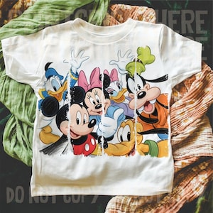 May include: White t-shirt featuring a colorful graphic of Disney characters including Mickey Mouse, Minnie Mouse, Donald Duck, Daisy Duck, and Goofy. The design has a distressed, vintage look.