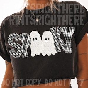 May include: A black cropped t-shirt featuring the word SPOOKY in a black and white gingham pattern. The two letter O's are replaced by white ghost figures with black eyes. The shirt has a crew neckline and short sleeves with a raw hem finish.