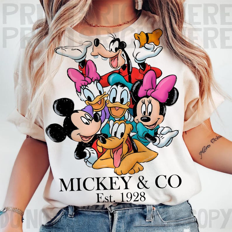 May include: Cream-colored t-shirt featuring a graphic of Mickey Mouse, Minnie Mouse, Donald Duck, Daisy Duck, Goofy, and Pluto. The text "MICKEY & CO" and "Est. 1928" are printed below the characters. The design is a colorful cartoon.