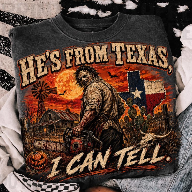 Puede incluir: Una sudadera gris oscuro con un gr&aacute;fico de un personaje sosteniendo una motosierra en un entorno rural con un molino, un granero, una calabaza, un cactus y la bandera de Texas. El texto dice HE'S FROM TEXAS, I CAN TELL en una fuente desgastada.