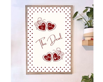 Puede incluir: Una impresión enmarcada con un fondo crema y un borde de lunares rojos. La impresión presenta las palabras "The Deal" en cursiva, junto con dos conjuntos de diseños en forma de corazón con nombres y números. Una guitarra está en uno de los corazones.