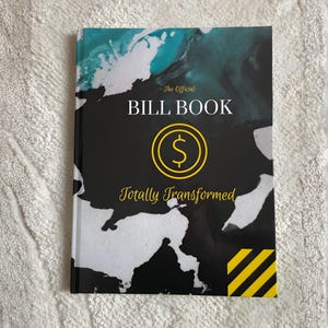 May include: A hardcover bill book with a black cover featuring the text "The Official BILL BOOK" and "Totally Transformed." A yellow dollar sign is in the center. The cover has a teal and white abstract design.