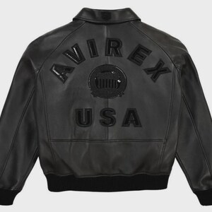 May include: Black leather jacket with the word "AVIREX" arched across the shoulders and "USA" below a circular emblem. The jacket has a ribbed hem and cuffs. The back of the jacket is the focus of the image.
