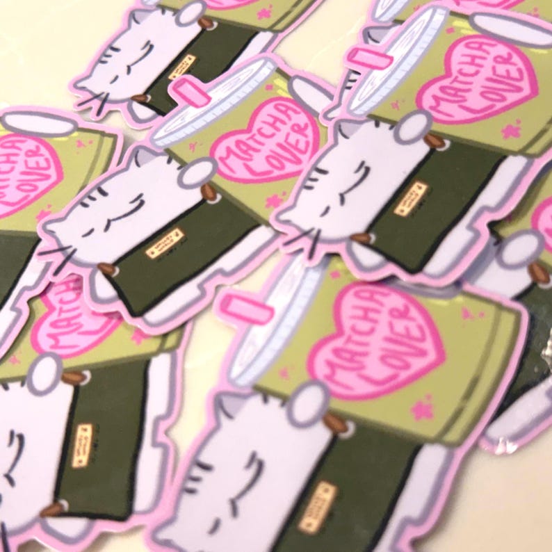 Op de afbeelding: Een verzameling gestanste stickers met een witte kat met grijze strepen die een groen matchadrankje in een doorzichtige beker vasthoudt. De beker heeft een roze hartje met de tekst MATCHA LOVER. De kat heeft een kalme uitdrukking.