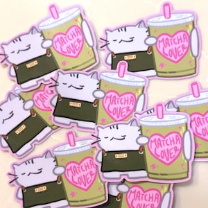 Op de afbeelding: Een verzameling gestanste stickers met een lichtpaarse kat die een donkergroen schort draagt en een lichtgroene beker met een roze rietje vasthoudt. De beker toont een roze hart met de tekst MATCHA LOVER in roze letters geschreven.