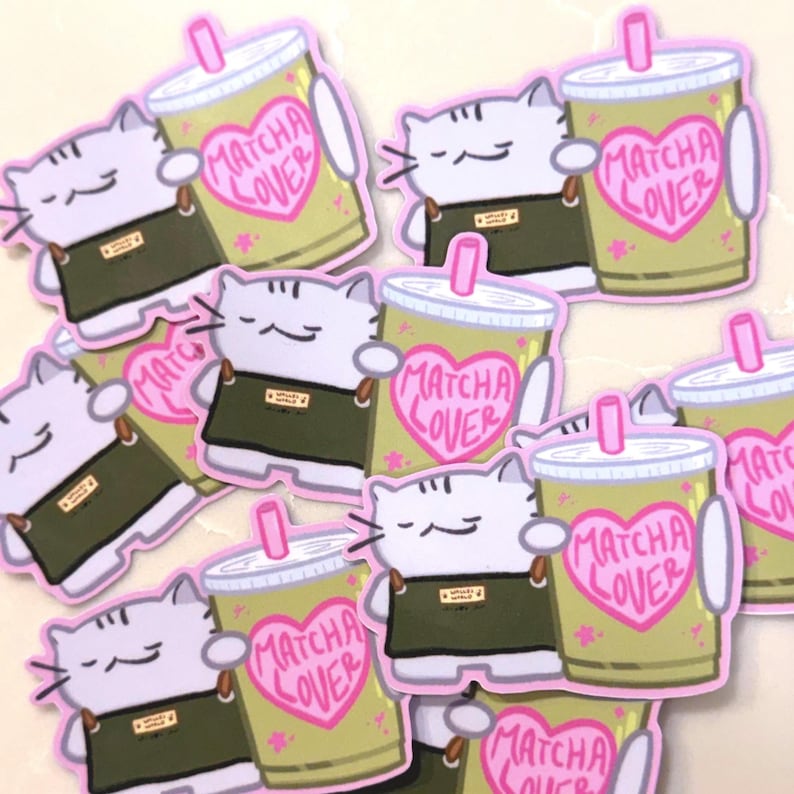Op de afbeelding: Een verzameling gestanste stickers met een lichtpaarse kat die een donkergroen schort draagt en een lichtgroene beker met een roze rietje vasthoudt. De beker toont een roze hart met de tekst MATCHA LOVER in roze letters geschreven.