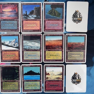 May include: A collection of fantasy art trading cards featuring various landscapes, including mountains, islands, and deserts. The cards have a brown border and include text. A white card with the text "CZECH MATE" and a logo is also present.