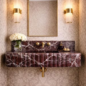 Puede incluir: Un lujoso baño con un lavabo de mármol burdeos y grifos dorados. El lavabo tiene un diseño acanalado y está colocado contra un papel pintado floral. Un espejo con marco dorado y apliques completan el elegante aspecto.