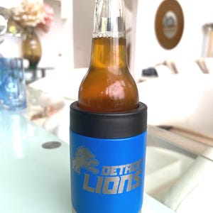 Show your football pride and keep your favorite drink ice cold with this Detroit Lions-inspired 12 oz insulated bottle cooler. Featuring a laser-engraved design on a durable, powder-coated blue finish, it combines style, function, and team spirit in one premium game day accessory. The double-wall stainless steel insulation keeps drinks at the perfect temperature longer, making it ideal for tailgates, backyard barbecues, camping trips, man caves, or just relaxing while watching the big game.