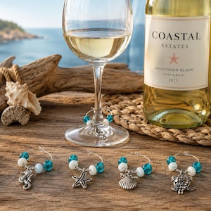 May include: A set of four silver-toned metal wine glass charms featuring sea-themed pendants including a seahorse, starfish, seashell, and sea turtle. Each charm is accented with round turquoise and white beads on a circular wire hoop.