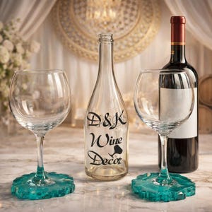 May include: A wine-themed still life featuring two clear wine glasses with teal bases, a clear bottle with "D&K Wine Decor" text, and a bottle of red wine. The background includes a floral arrangement and draped fabric.