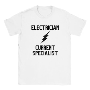 以下が含まれることがあります： 白のTシャツ。黒い文字で「電気技師、電流スペシャリスト」と書かれ、黒い稲妻のグラフィックがあります。Tシャツはクルーネックです。