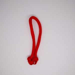 May include: A bright red cord loop with a knotted base. The cord is thick and appears to be made of a durable material. The loop is in a vertical position against a white background.