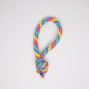 Könnte beinhalten: Eine bunte, geknotete Seilschlaufe. Das Seil besteht aus ineinander verwobenen Strängen in Regenbogenfarben, darunter Rot, Gelb, Grün und Blau. Der Knoten ist fest gesichert und die Schlaufe hat eine Tropfenform.