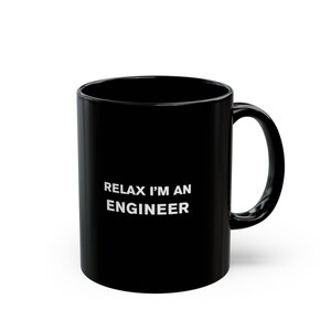 Puede incluir: Una taza de café de cerámica negra con la inscripción blanca "RELAX I'M AN ENGINEER". La taza tiene un asa curva y un acabado brillante. Perfecta para ingenieros.