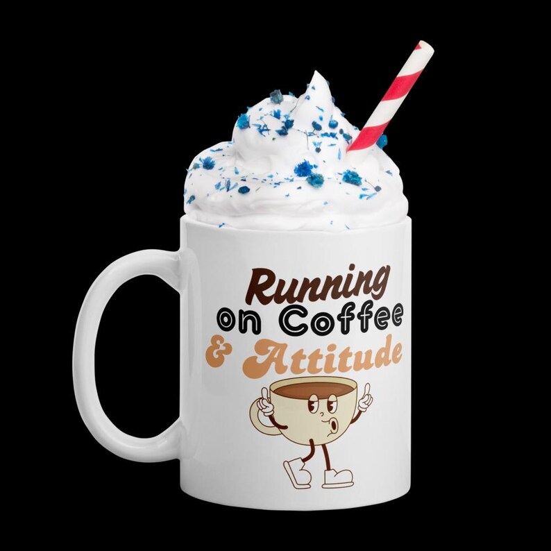 May include: White coffee mug with the text "Running on Coffee & Attitude" and a cartoon coffee cup character. The mug is topped with whipped cream, blue sprinkles, and a red and white striped straw.