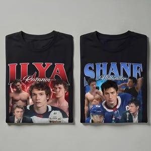 Peut inclure: Deux t-shirts noirs avec des graphiques de style vintage. Un t-shirt présente le nom "ILYA Rozanov" en rouge, avec des images d'un homme. L'autre t-shirt affiche "SHANE Hollander" en bleu, avec des images d'un homme. Les deux t-shirts ont un col rond.