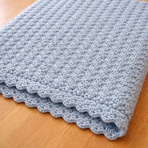 K&ouml;nnte beinhalten: Eine hellblaue H&auml;keldecke mit einem durchgehend strukturierten Stichmuster. Die R&auml;nder der Decke sind mit einer dekorativen Bogenkante versehen, was ein weiches und gleichm&auml;&szlig;iges Erscheinungsbild &uuml;ber das gesamte St&uuml;ck hinweg erzeugt.