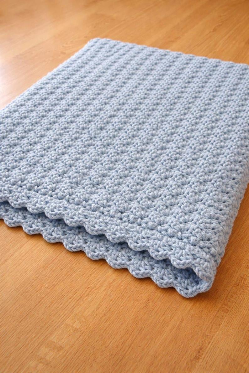 K&ouml;nnte beinhalten: Eine hellblaue H&auml;keldecke mit einem durchgehend strukturierten Stichmuster. Die R&auml;nder der Decke sind mit einer dekorativen Bogenkante versehen, was ein weiches und gleichm&auml;&szlig;iges Erscheinungsbild &uuml;ber das gesamte St&uuml;ck hinweg erzeugt.