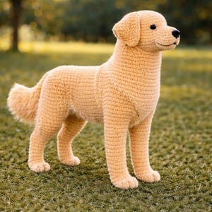 May include: A crocheted golden retriever dog stands on green grass. The handmade dog has a light tan color, with black eyes and nose. The dog's tail is fluffy, and its ears are floppy. The background is blurred with green and yellow tones.