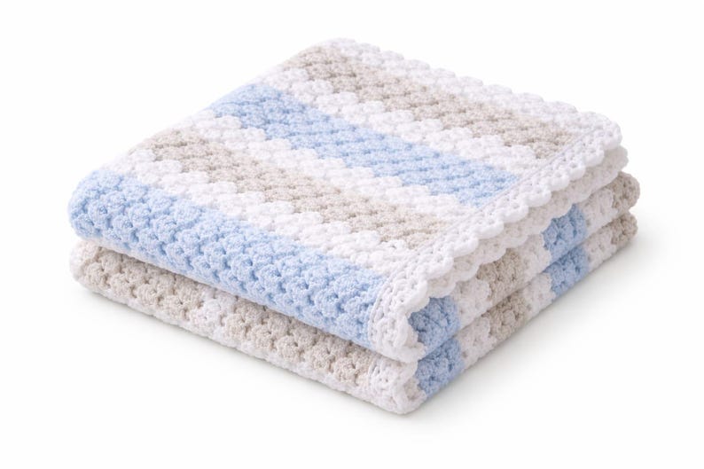 K&ouml;nnte beinhalten: Eine gefaltete H&auml;keldecke mit einem strukturierten Muster aus abwechselnden diagonalen Streifen in Wei&szlig;, Hellblau und Beige. Die Decke ist mit einem zarten, wei&szlig;en, wellenf&ouml;rmigen H&auml;kelrand an den Kanten versehen, was f&uuml;r ein weiches Erscheinungsbild sorgt.