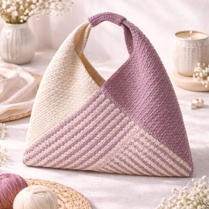 May include: A handmade, triangular tote bag in cream and lavender. The bag features a striped pattern in cream and lavender, with a solid lavender section. The handle is lavender. The bag is made of a textured material.