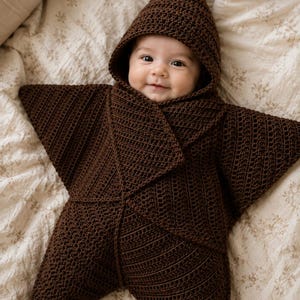 May include: A dark brown crocheted star-shaped swaddle blanket with a pointed hood. The garment features a textured stitch pattern and wraps around the body, creating five distinct points that extend outward from the center of the piece.