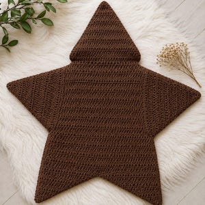 May include: A dark brown star-shaped crochet blanket featuring a pointed hood at the top. The item is constructed with a consistent stitch pattern throughout, creating a textured surface that forms five distinct points in a classic star silhouette.