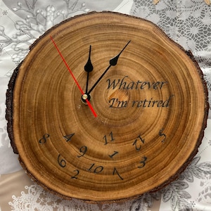 Può includere: Un orologio rotondo in legno con finitura a venatura naturale. Il quadrante presenta numeri neri, lancette nere e una lancetta dei secondi rossa. Il testo "Whatever I'm retired" è inciso sul quadrante.