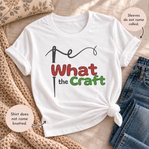 May include: A white short-sleeve t-shirt featuring a black needle graphic and the text What the Craft in red and green lettering. The shirt includes text notes stating that the sleeves do not come rolled and the shirt does not come knotted.