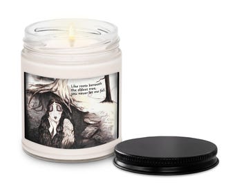 Puede incluir: Una vela blanca en un tarro de cristal con tapa negra. La vela tiene una etiqueta con una ilustración en blanco y negro de una mujer bajo un árbol, con el texto "Como raíces bajo el árbol más antiguo, nunca me dejas caer."