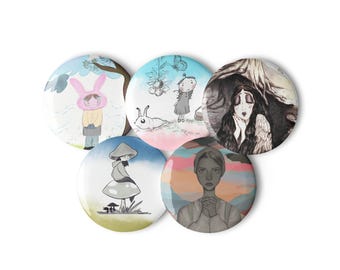 Puede incluir: Un conjunto de cinco chapas redondas con diversas ilustraciones. Una muestra a una persona con gorro de conejo rosa, otra una figura con un caracol, una una persona de pelo oscuro en una cueva, una sobre una seta y una con las manos juntas.