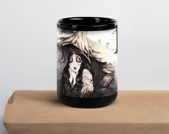 Puede incluir: Taza de cerámica negra con una ilustración en escala de grises de una mujer con largo cabello negro, alas de ángel y ojos cerrados, bajo un árbol. La obra de arte está detallada con reflejos blancos. La taza está colocada sobre una superficie de madera.
