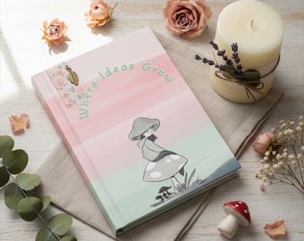 Puede incluir: Un diario de tapa dura con rayas en rosa y verde pastel, que presenta una ilustración de líneas de una persona con un sombrero de seta, el texto "Where Ideas Grow" y un pequeño dije de hoja dorada en la esquina superior izquierda.