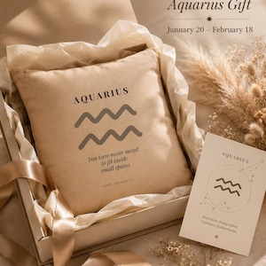 Può includere: Un cuscino beige con la parola "AQUARIUS" e un simbolo ondulato, in una confezione regalo con una carta con la scritta "AQUARIUS". Il testo "Perfect Aquarius Gift" è in alto, con le date 20 gennaio - 18 febbraio.