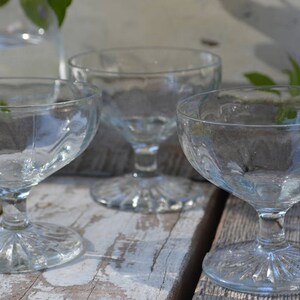 Puede incluir: Tres copas de postre de vidrio transparente con un dise&ntilde;o acanalado y un tallo corto. Las copas est&aacute;n dispuestas sobre una superficie de madera.