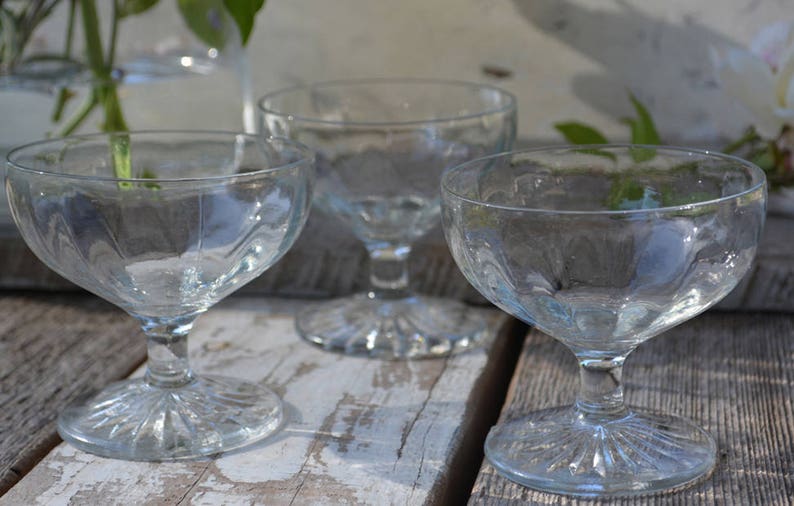 Puede incluir: Tres copas de postre de vidrio transparente con un dise&ntilde;o acanalado y un tallo corto. Las copas est&aacute;n dispuestas sobre una superficie de madera.