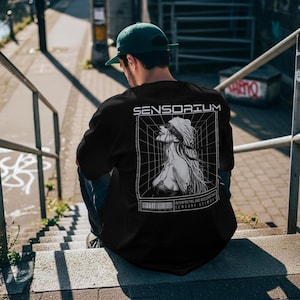 May include: Black t-shirt with the word "SENSORIUM" above a black and white graphic of a woman with a blindfold. The graphic is inside a grid, with text below that reads "INTERPRETING AND INTEGRATING SENSORY STIMULI".