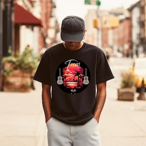 May include: Black t-shirt featuring a circular graphic with the word "Tocar" in script. The graphic includes a sunset scene with palm trees, guitars, and a red and orange sky. The shirt is a classic crew neck.