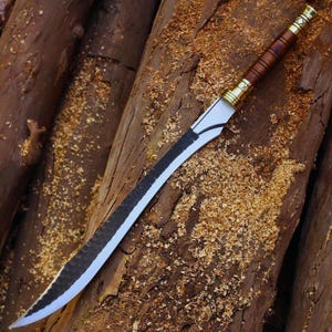 Puede incluir: Una espada larga con una hoja oscura y texturizada que presenta un borde plateado pulido. El mango está hecho de madera marrón con detalles metálicos dorados en el pomo y la guarda, mostrando un diseño elegante y afilado con una punta aguda.