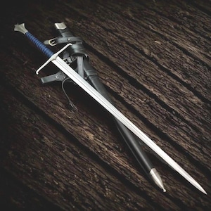 May include: A longsword with a silver-toned crossguard and pommel, featuring a blue cord-wrapped grip. The blade is straight and double-edged. It is accompanied by a black leather scabbard with silver-toned metal fittings and black leather straps.