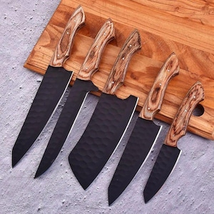 May include: A set of five kitchen knives with matte black hammered blades and light brown wood grain handles. The knives vary in size and blade shape, featuring pointed tips and curved edges, arranged in a row on a wooden cutting board.