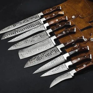May include: A set of eight kitchen knives with Damascus steel blades featuring a wavy, layered pattern and dark brown wooden handles with silver rivets. The knives are arranged in a diagonal row, partially resting on a brown leather roll.
