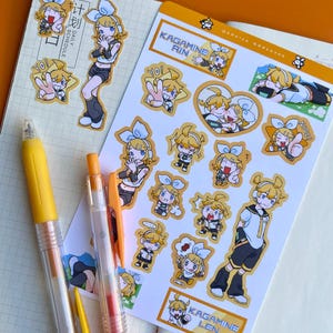 May include: A collection of anime-style stickers featuring characters with yellow hair and blue bows. The stickers are on a white background with text that reads "Kagamine Rin" and "Kagamine Len". Two yellow pens are in the foreground.